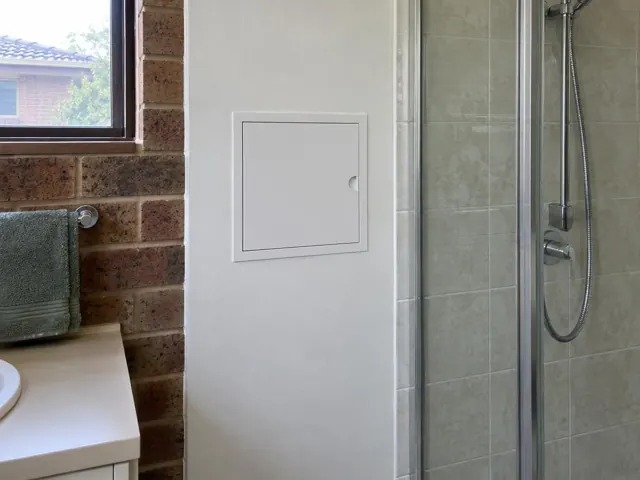 Bathroom wall with a small access panel beside a shower and tiled brick feature wall in Quakers Hill